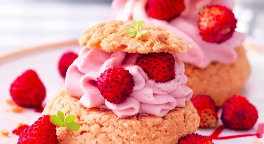 Deliziosa mousse di fragole su bignè, guarnita con fragoline di bosco e foglioline verdi.