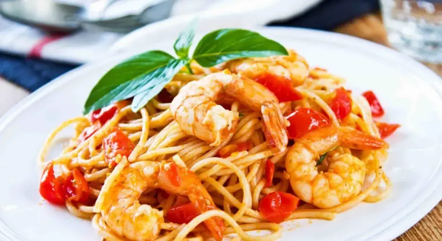 Un piatto invitante di spaghetti con gamberetti succulenti e pomodorini freschi, guarnito con basilico.