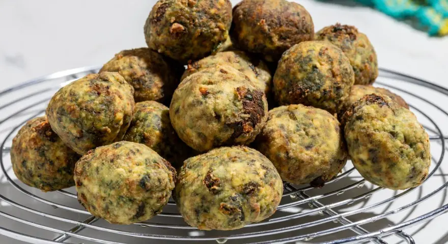 Pile di polpette ricotta e spinaci dorate e appetitose su una griglia metallica.
