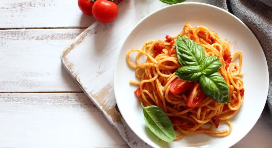 Spaghetti al sugo di pomodoro fresco, guarniti con basilico e pomodorini, su un piatto bianco.
