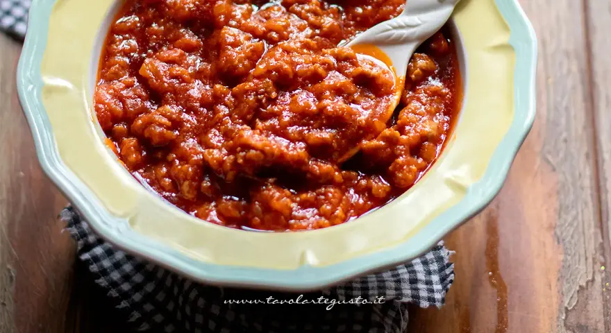 Un invitante sugo con salsiccia, denso e saporito, servito in una ciotola gialla con un cucchiaio decorato.