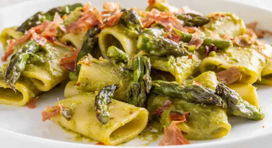 Paccheri conditi con una cremosa salsa verde e asparagi selvatici, guarniti con croccante prosciutto.