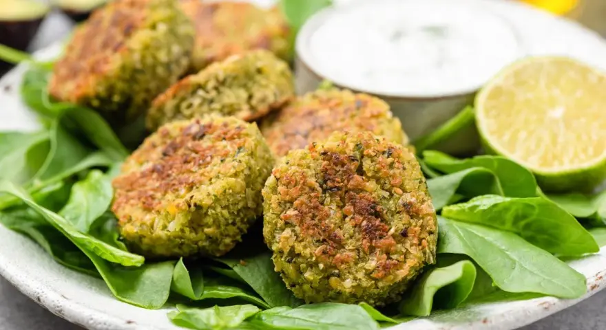 Deliziose polpette di spinaci dorate, servite su un letto di spinacini freschi con salsa e spicchi di lime.