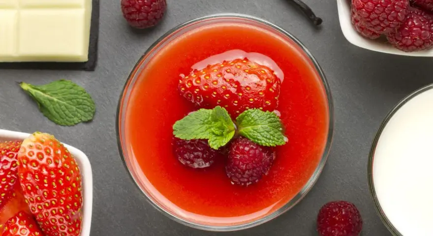 Un bicchiere di coulis di fragole con fragola, lamponi e menta. Accanto, fragole fresche, cioccolato bianco, lamponi e un bicchiere di latte.