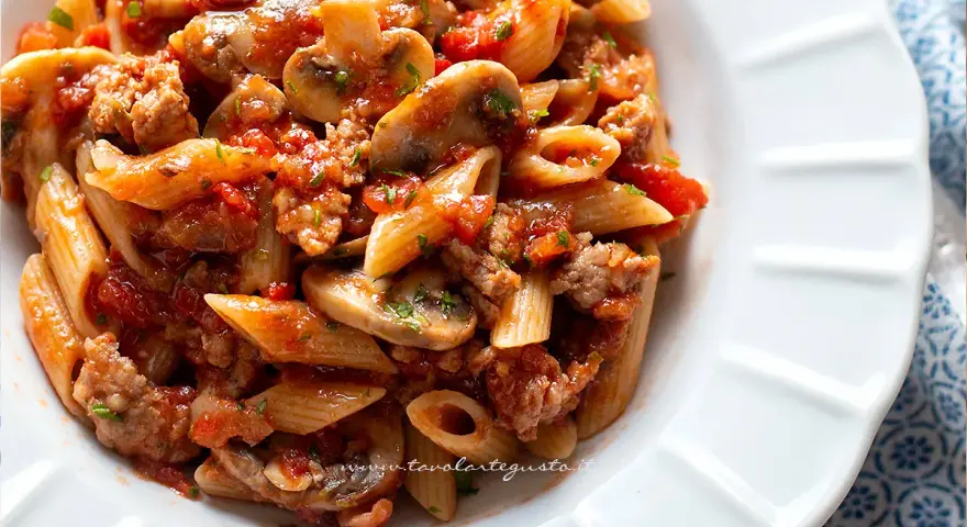 Piatto di pasta alla boscaiola con penne, funghi, salsiccia e pomodoro, condita con prezzemolo fresco.