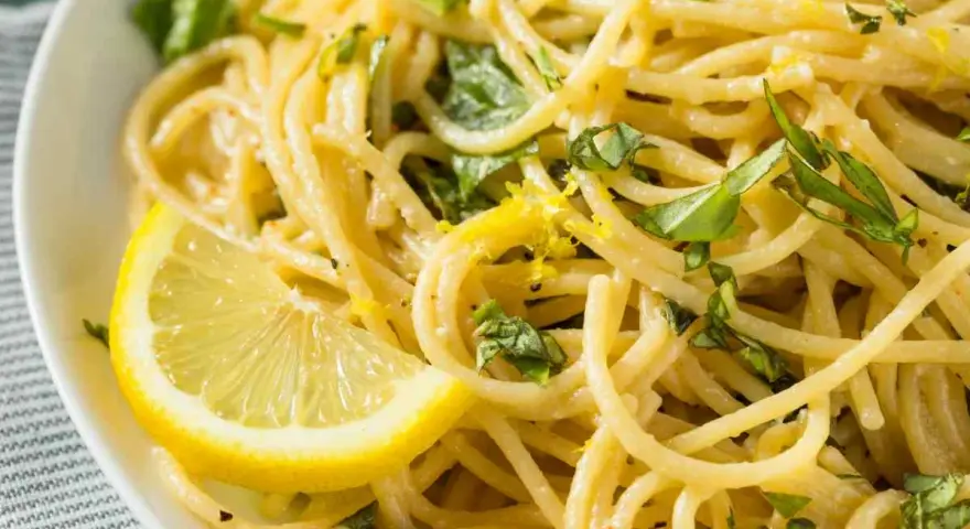 Un piatto invitante di spaghetti al limone, guarnito con scorza di limone e basilico fresco.