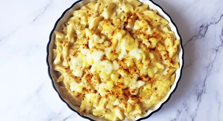 Piatto di mac and cheese fumante, con pasta penne cremosa e formaggio fuso, spolverato con paprika.