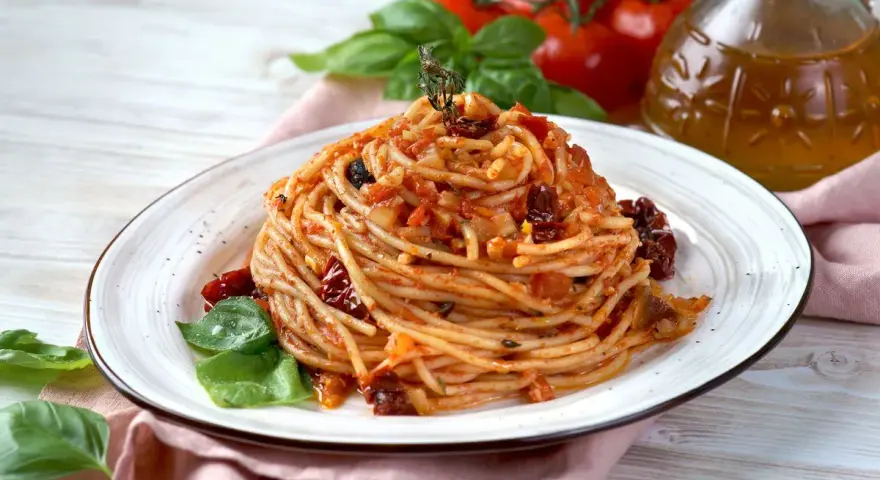 Un piatto di spaghetti conditi con un sugo rosso ricco di pomodori secchi, aglio e basilico fresco.