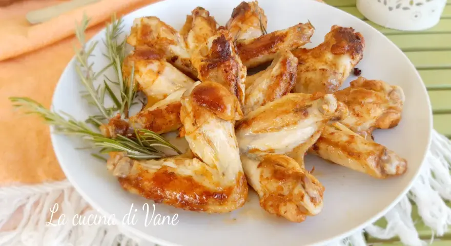 A plate of golden-brown, juicy chicken wings garnished with rosemary sprigs.