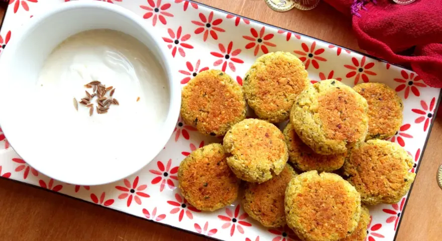 Falafel al forno dorati su un piatto decorato, accompagnati da una ciotola di salsa bianca con semi di cumino.