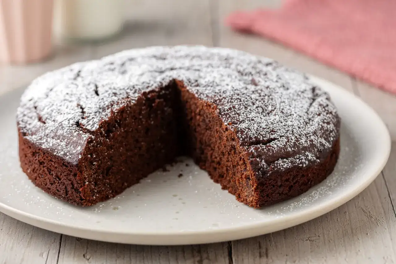 Torta al cioccolato soffice e spolverata di zucchero a velo, con una fetta mancante, pronta per essere gustata.