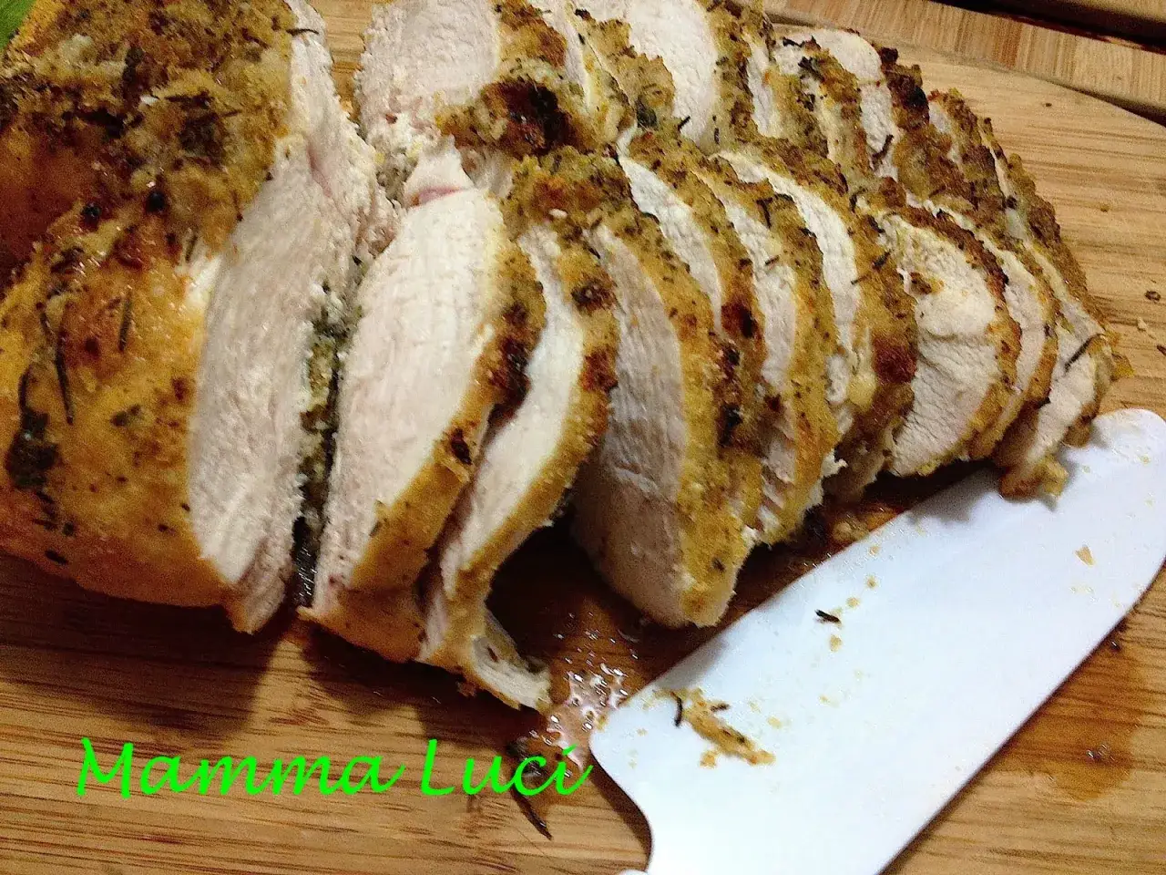 Petto di pollo al forno, succulento e dorato, tagliato a fette su un tagliere di legno. Un coltello bianco è appoggiato accanto.