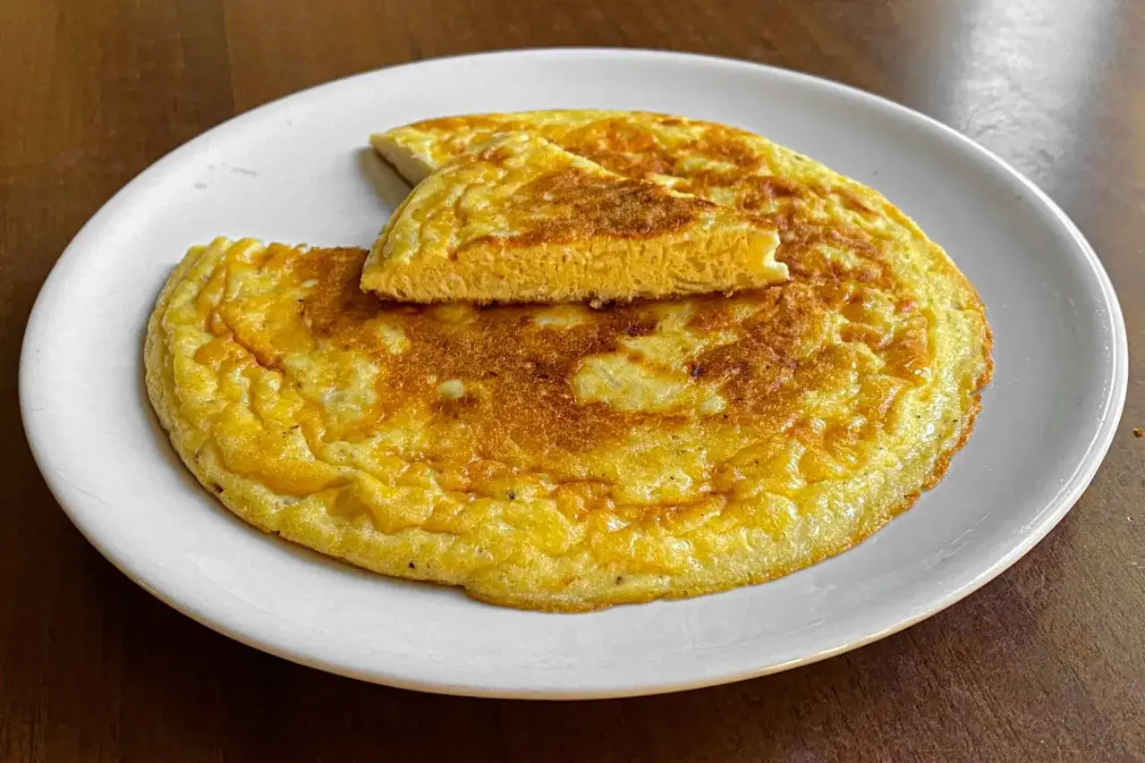 Frittata di cipolle dorata e soffice su un piatto bianco, con una fetta sollevata che mostra la consistenza interna.