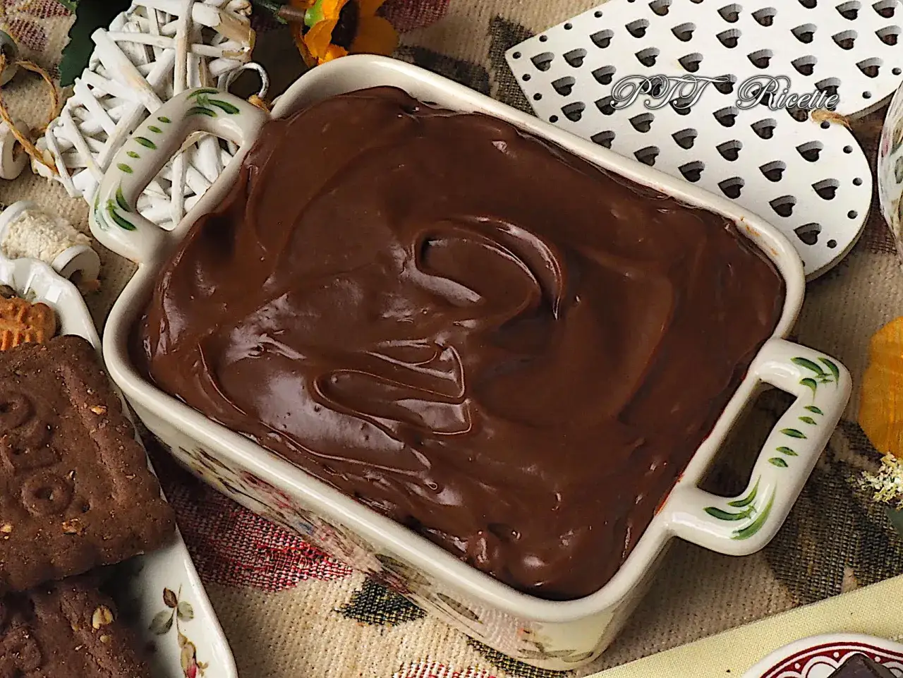 Crema pasticcera al cioccolato, liscia e invitante, in una ciotola decorata, pronta per essere gustata con biscotti.
