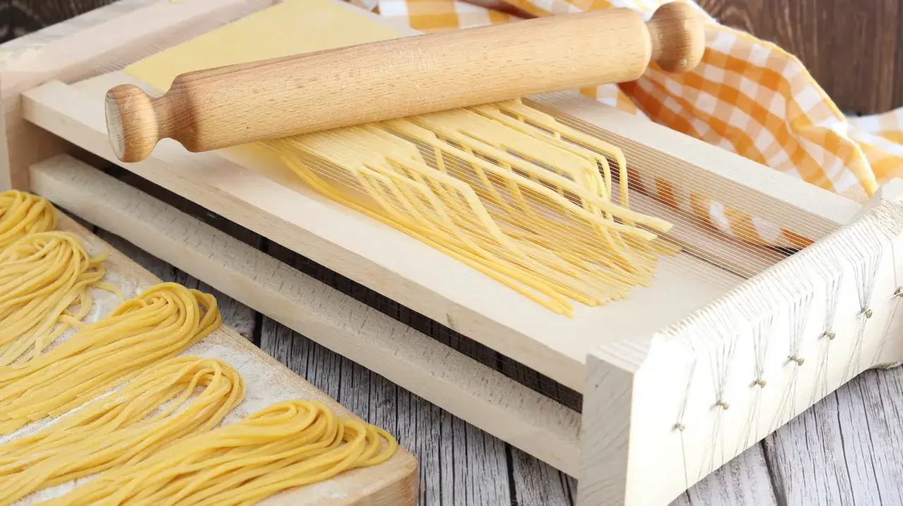 Pasta fresca tagliata con la chitarra, pronta per essere cucinata. Un rotolo di legno e un canovaccio a quadretti completano la scena.