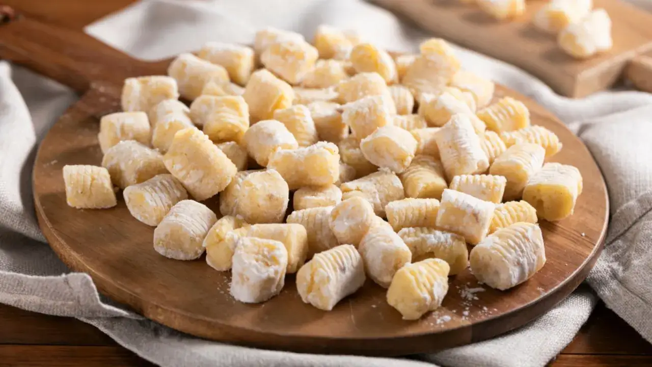 Un mucchio di deliziosi gnocchi senza glutine, spolverati di farina, pronti per essere cucinati su un tagliere di legno.