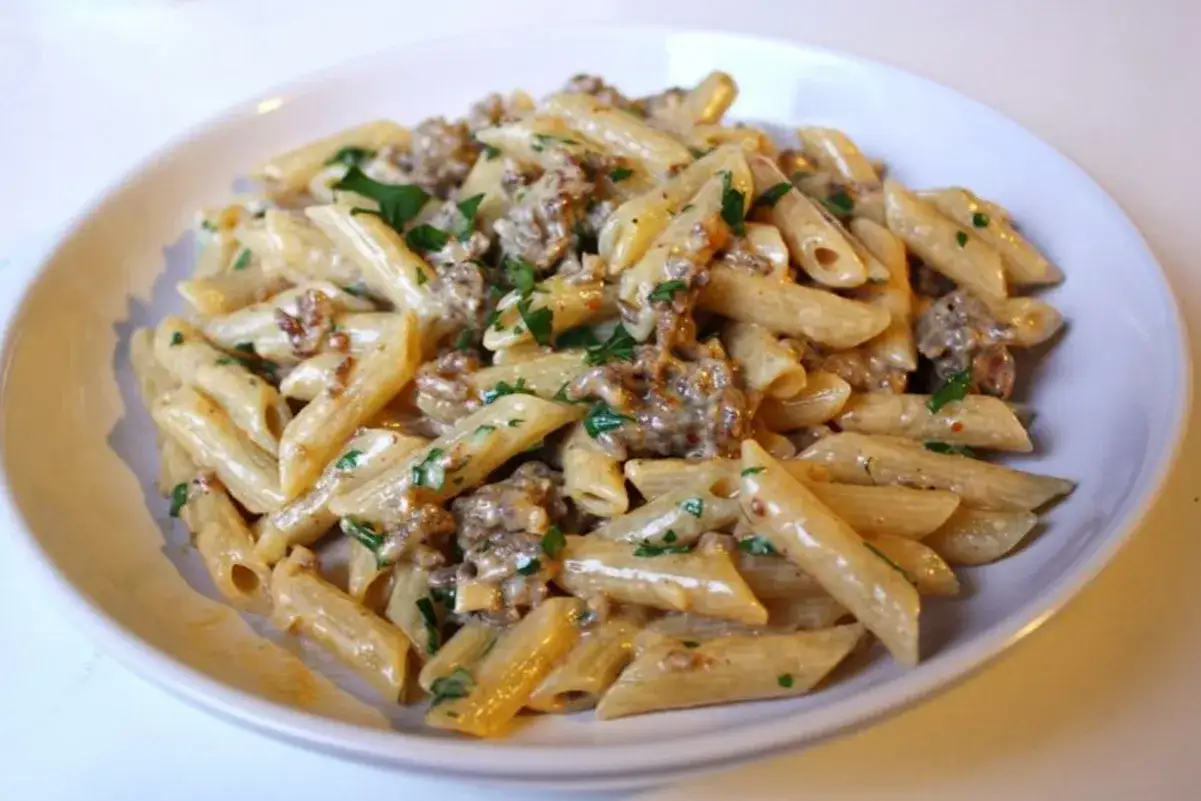 Penne al sugo con salsiccia, un piatto cremoso e saporito, guarnito con prezzemolo fresco.