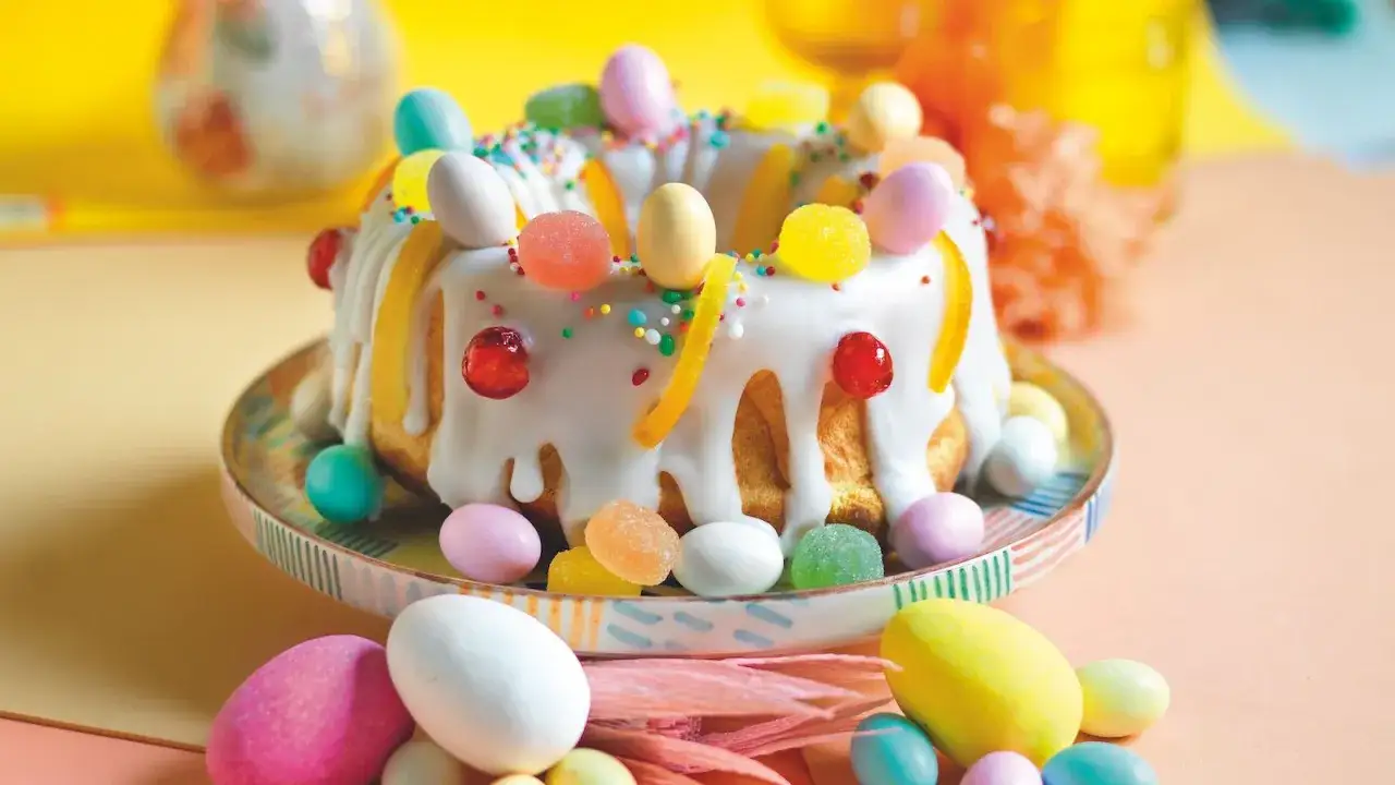 Un colorato dolce di Pasqua, decorato con uova di cioccolato, caramelle gommose e scorze d'arancia, su un piatto festivo.