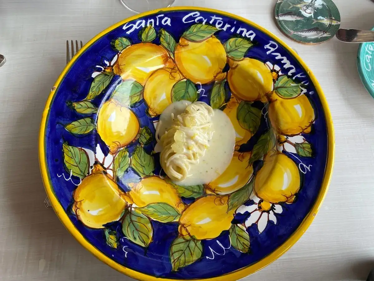 Un piatto di spaghetti al limone servito su un piatto decorato con limoni gialli e foglie verdi.