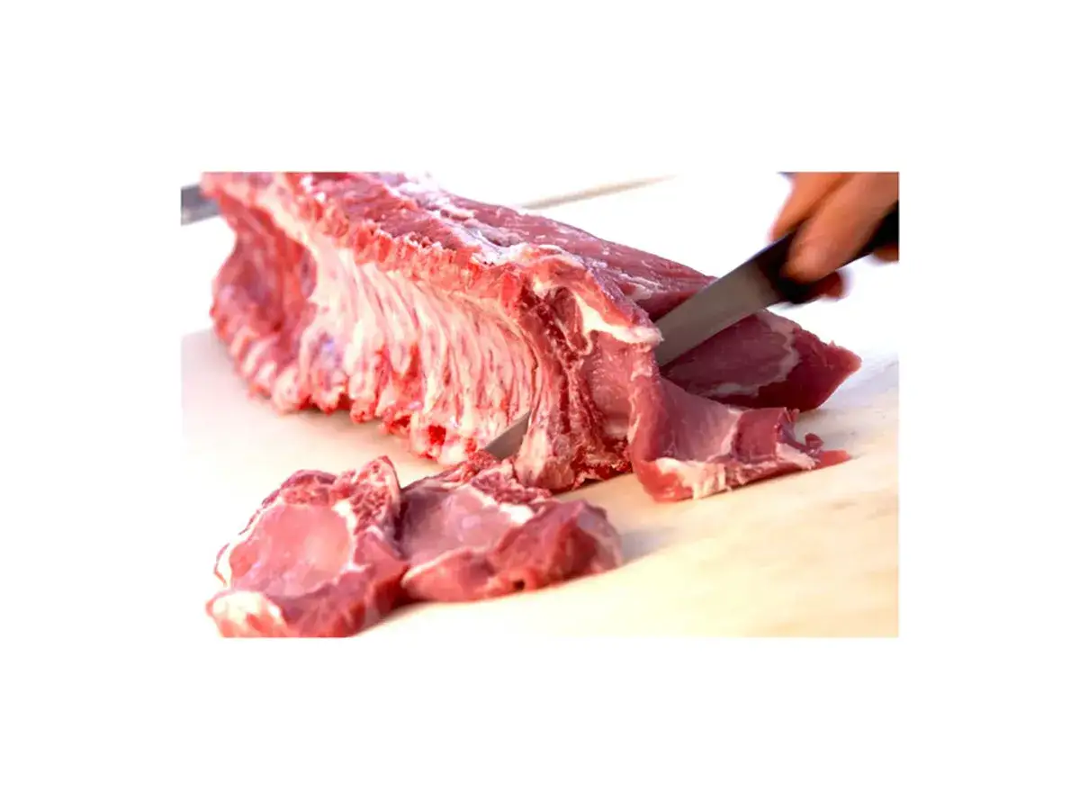 Una mano affilata taglia delle succulente braciole di maiale da una costata fresca su un tagliere di legno.