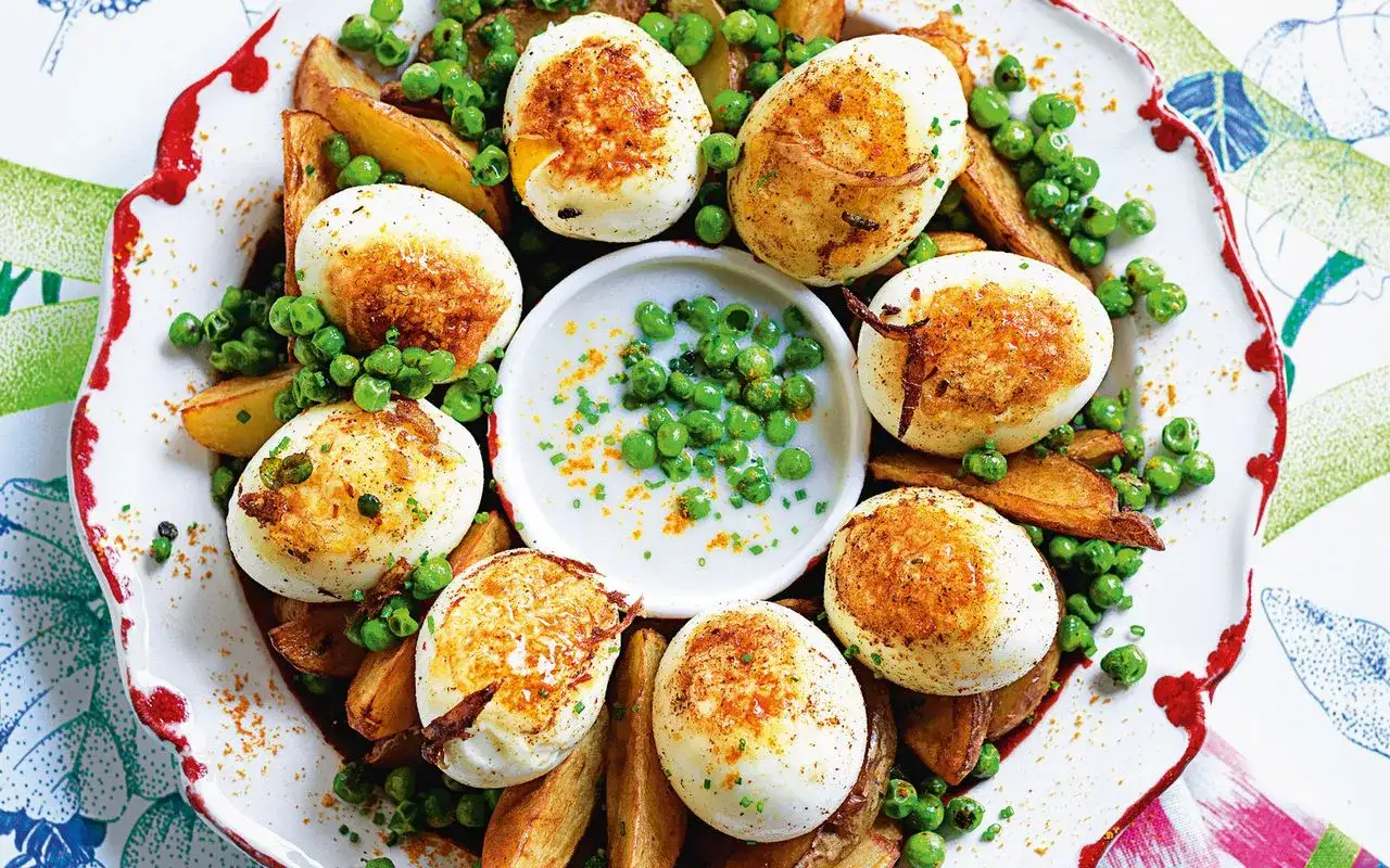 Uova ripiene per Pasqua, dorate e servite con patate arrosto e piselli freschi, un piatto colorato e gustoso.