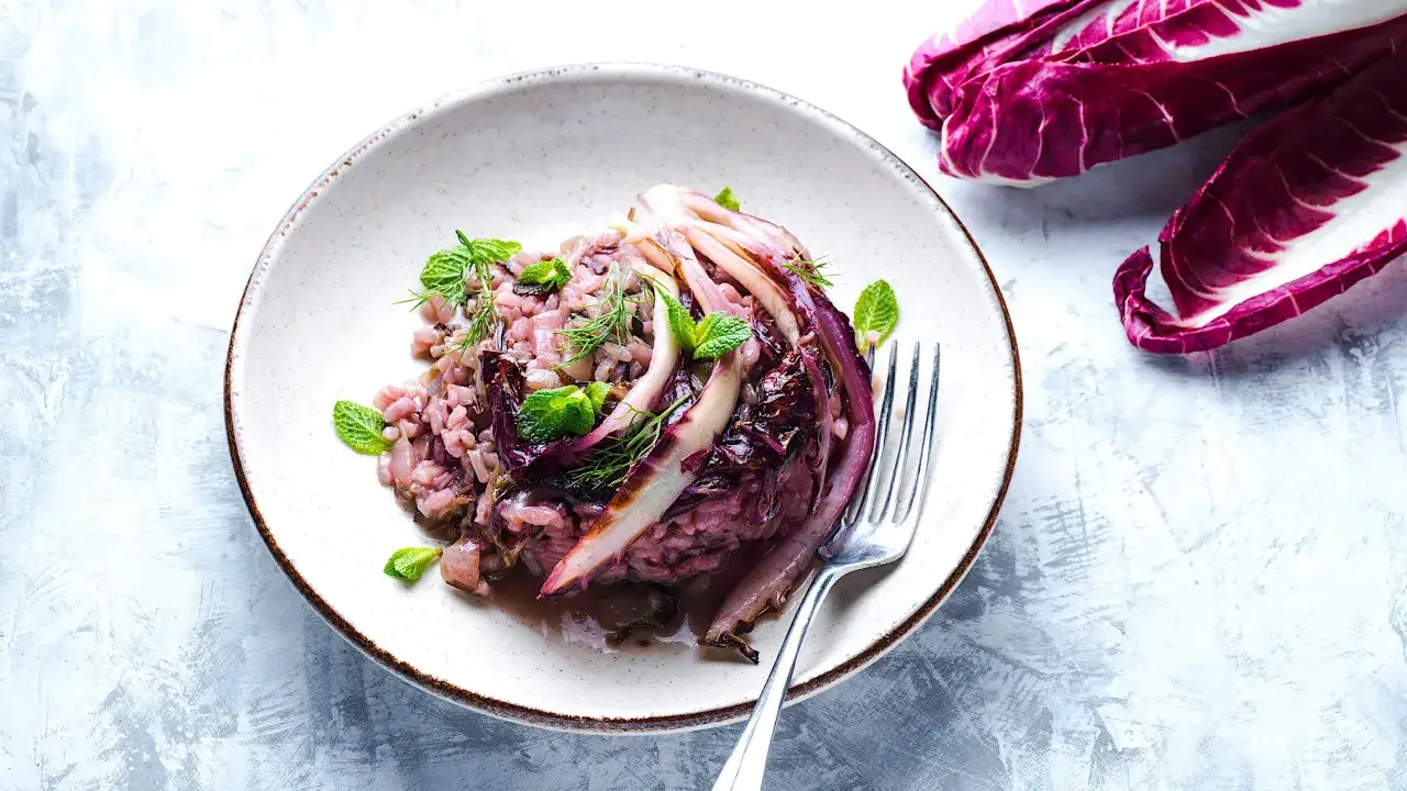 Un cremoso risotto al radicchio, guarnito con foglie di menta e aneto, pronto per essere gustato.