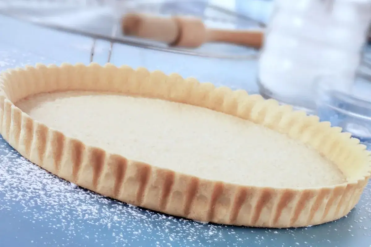 Base per crostata pronta, una deliziosa pasta frolla senza uova, cosparsa di zucchero a velo su un piano blu.