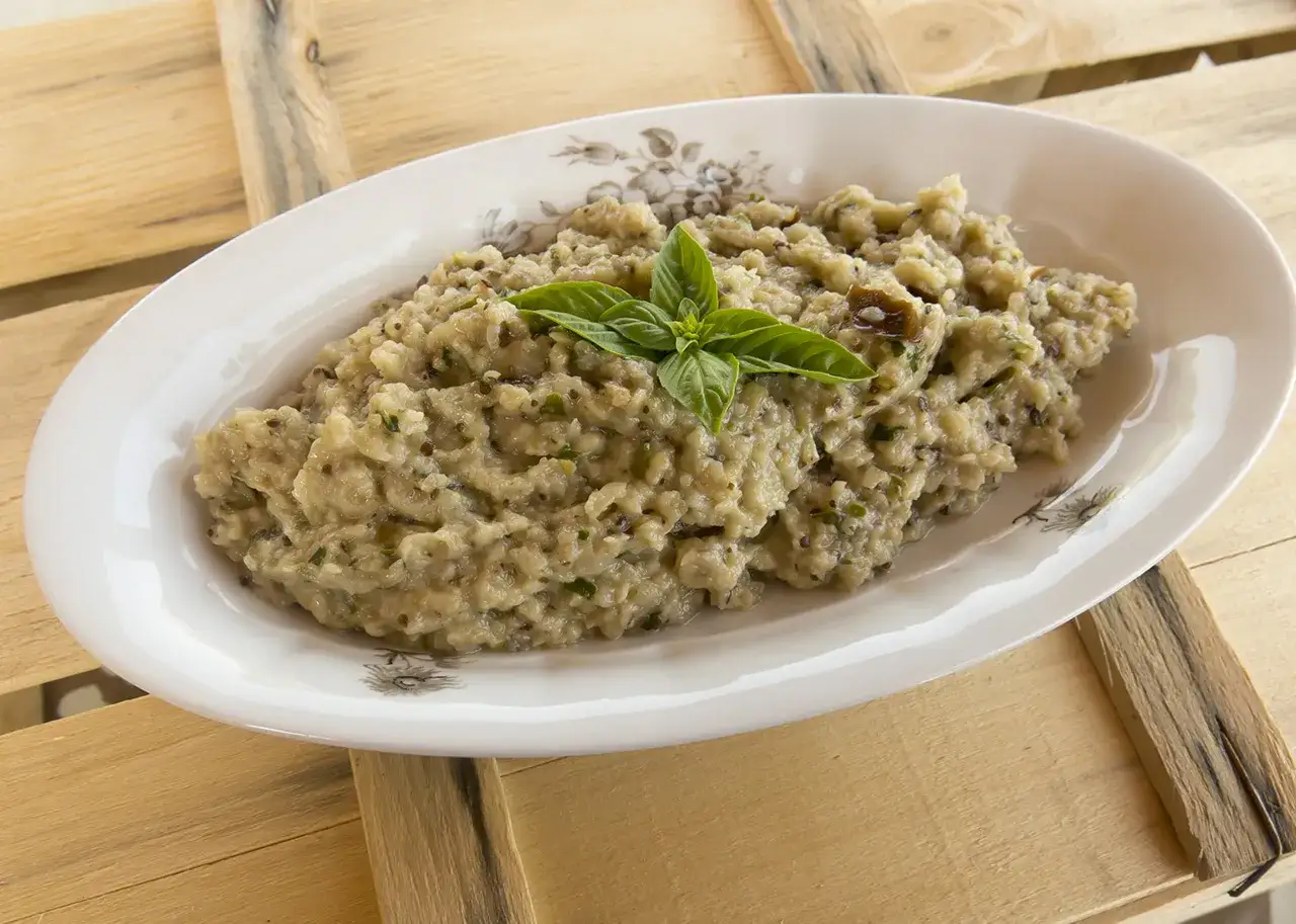 Crema di melanzane rustica, guarnita con basilico fresco, servita in un piatto ovale su un tavolo di legno.