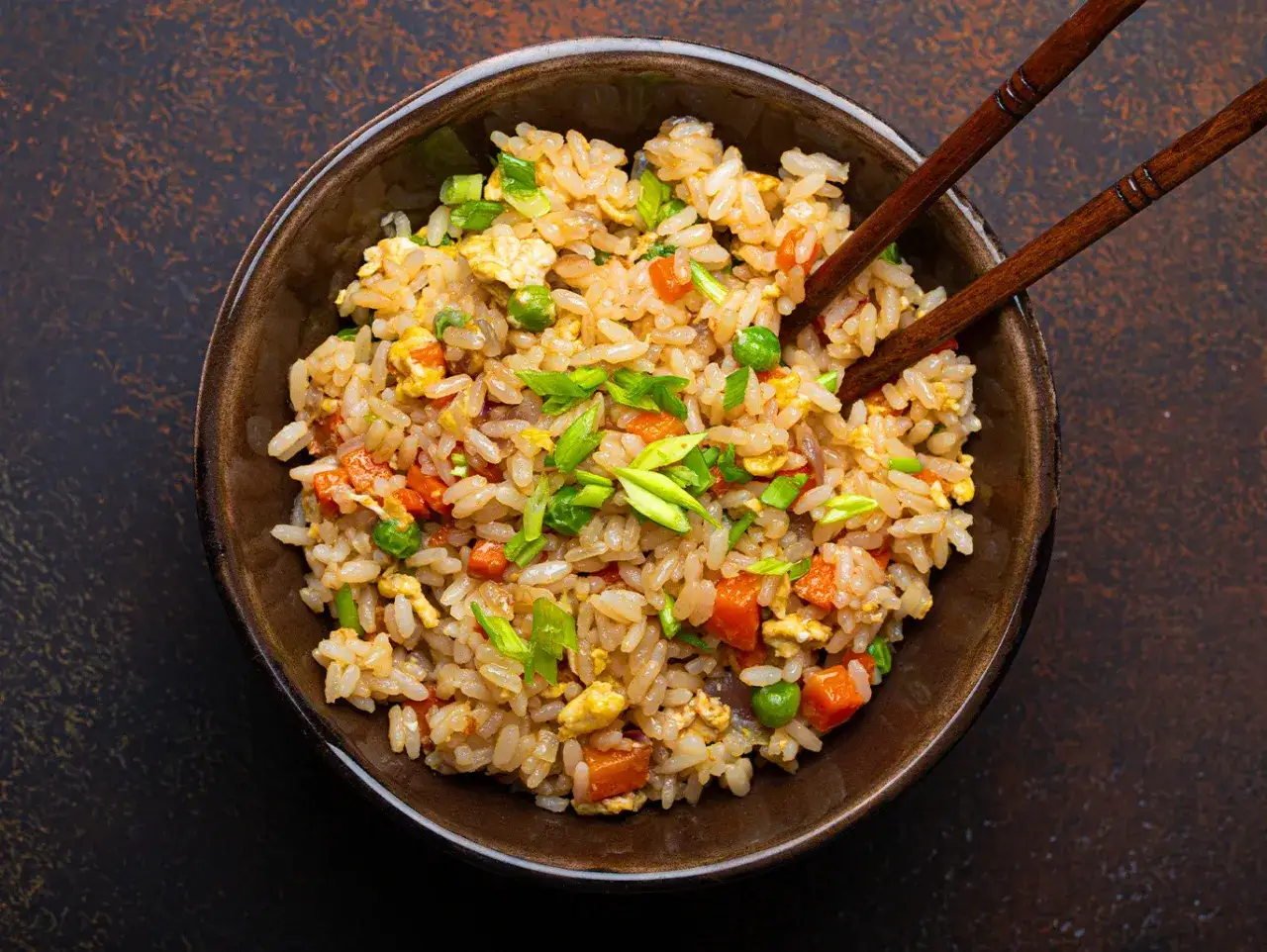 Un piatto fumante di riso alla cantonese, con piselli, carote, uova e cipollotto fresco, pronto per essere gustato con le bacchette.