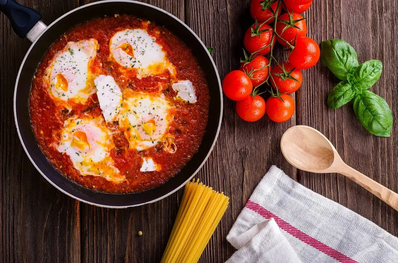 Uova al pomodoro in padella, con pomodorini freschi, basilico e spaghetti.