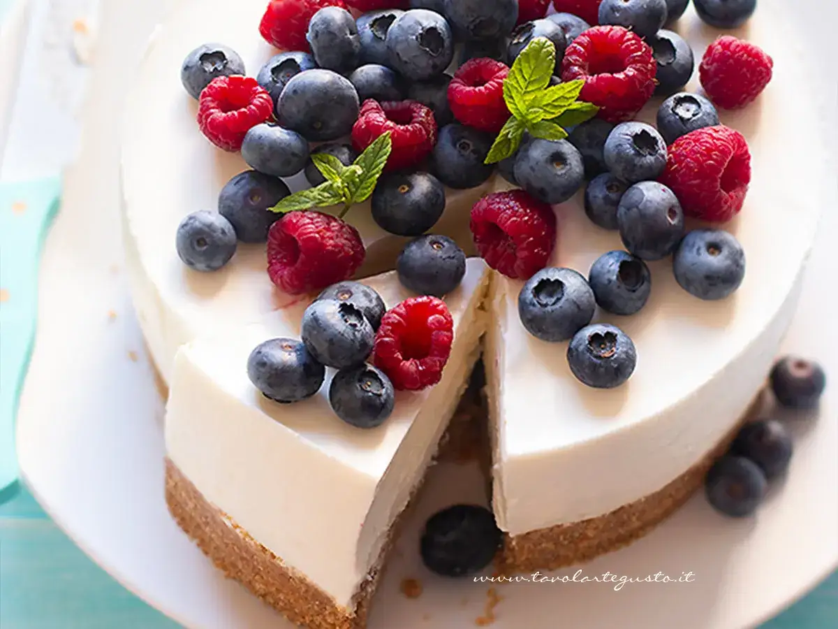 Cheesecake yogurt greco con frutti di bosco freschi, una fetta &egrave; stata tagliata.