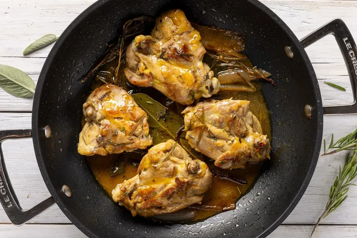 Cosce di pollo in padella, dorate e succulente, con erbe aromatiche e un sughetto invitante.