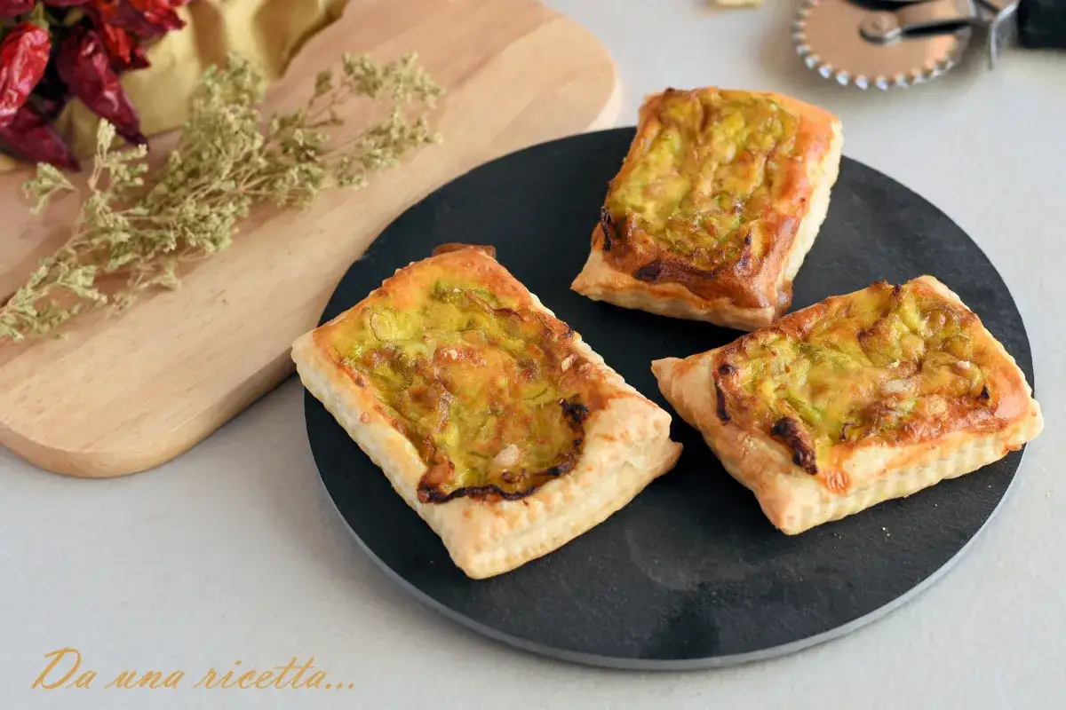 Tre tortine salate di pasta sfoglia con zucchine, dorate e invitanti, su un piatto nero.
