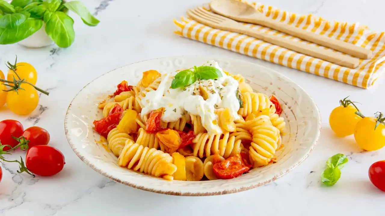 Fusilli con pomodorini e una generosa cucchiaiata di stracciatella, guarniti con basilico fresco.