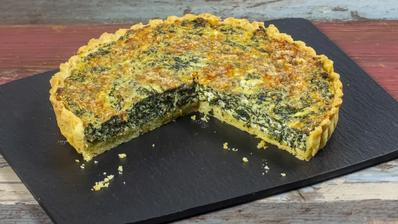 Torta salata ricotta e spinaci, dorata e invitante, servita su una pietra scura.