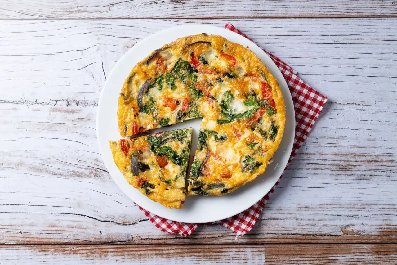 Frittata colorata con verdure, cotta in friggitrice ad aria, servita su un piatto bianco con tovagliolo a quadri rossi.