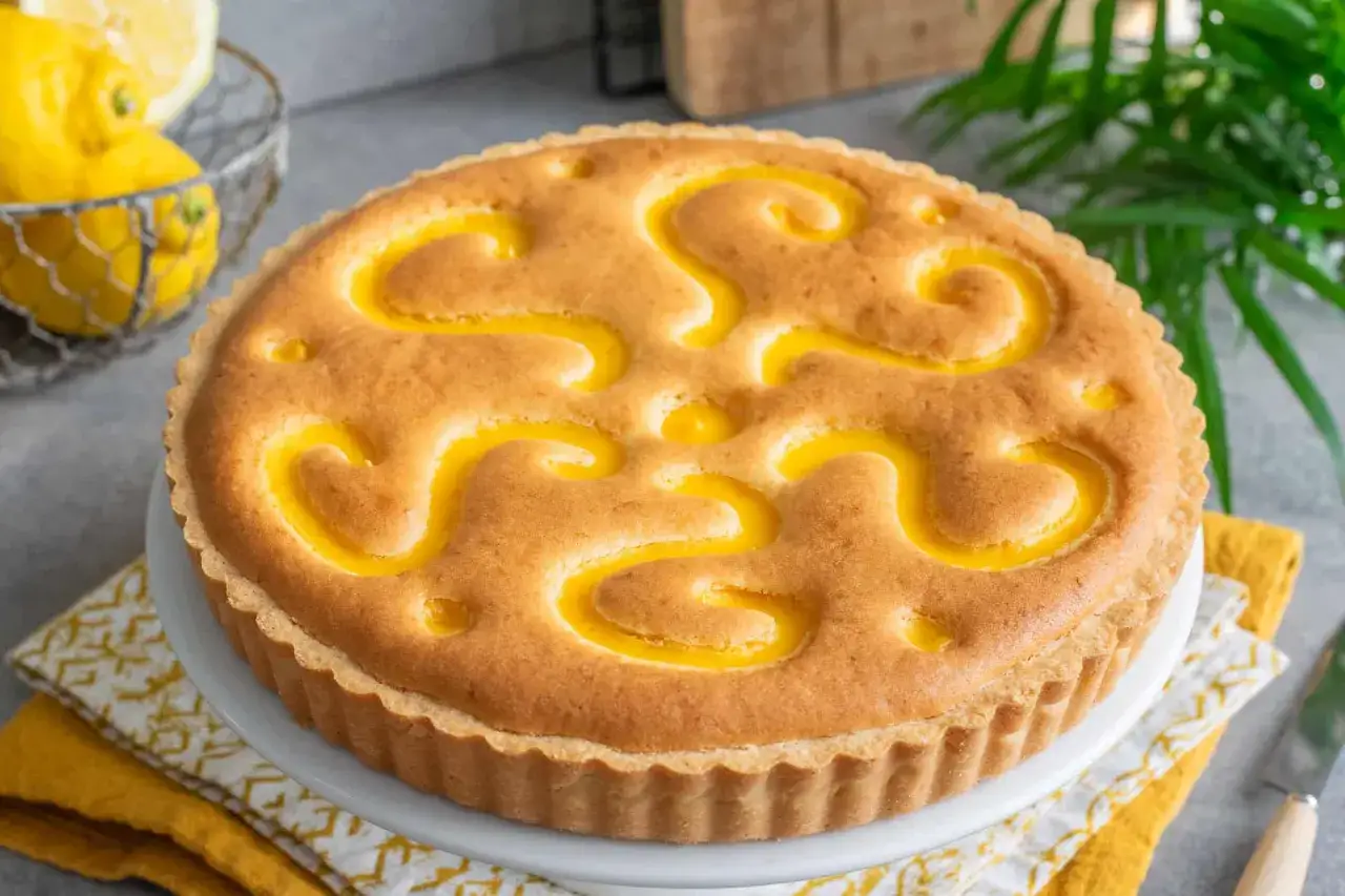 Deliziosa crostata al limone con un decoro a spirale dorato. Sullo sfondo, limoni freschi in un cestino.