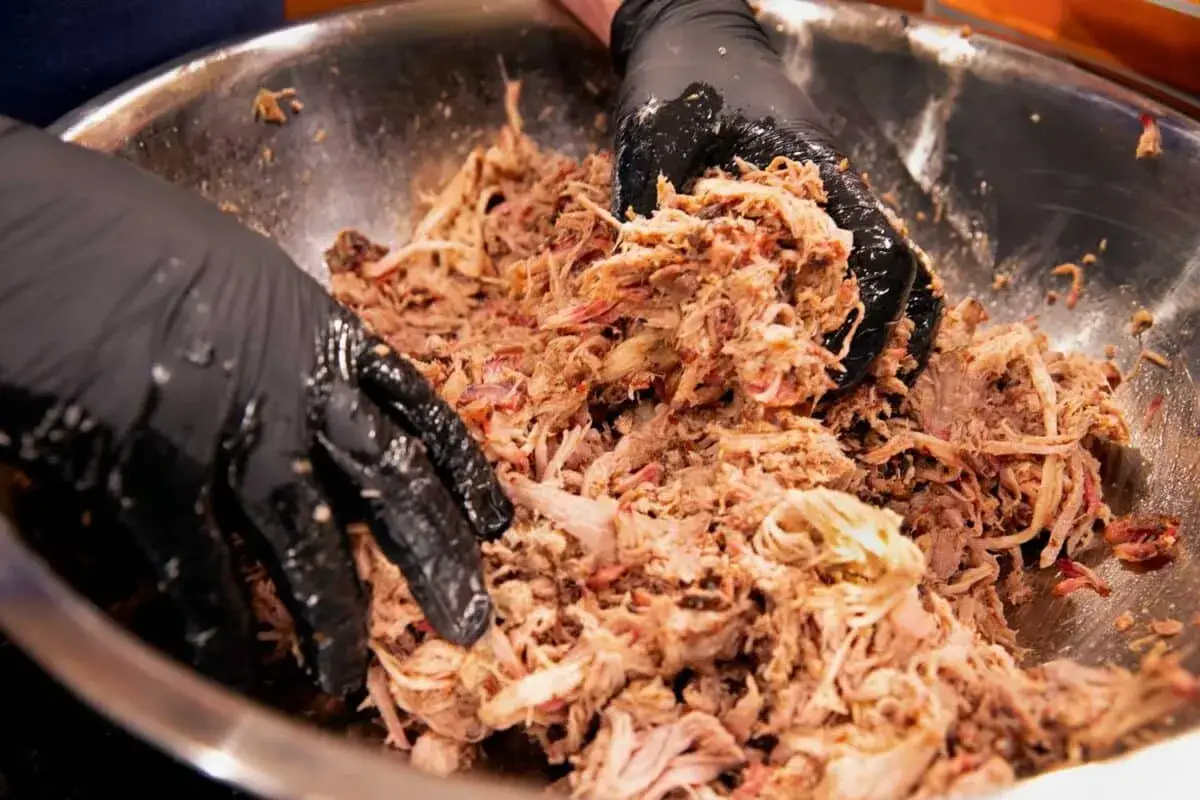 Mani guantate sfilacciano carne saporita per una perfetta pulled pork ricetta.