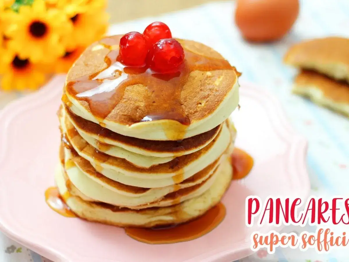 Pancake con albumi, soffici e dorati, inzuppati nello sciroppo d'acero e guarniti con ciliegie rosse.