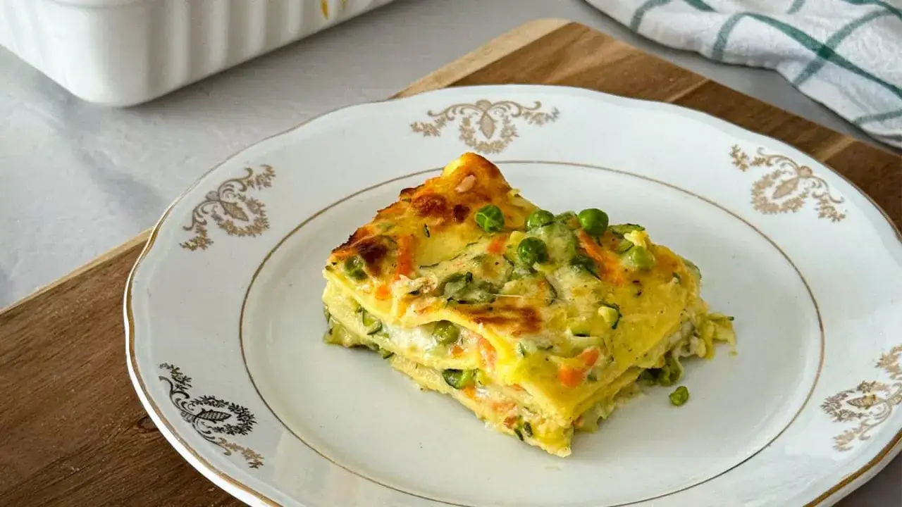 Una fetta di lasagne di verdure, con piselli e carote, su un piatto bianco decorato.