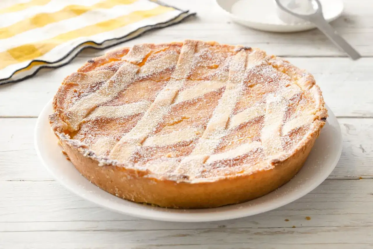 Pastiera napoletana con crema pasticcera, cosparsa di zucchero a velo, su un piatto bianco.