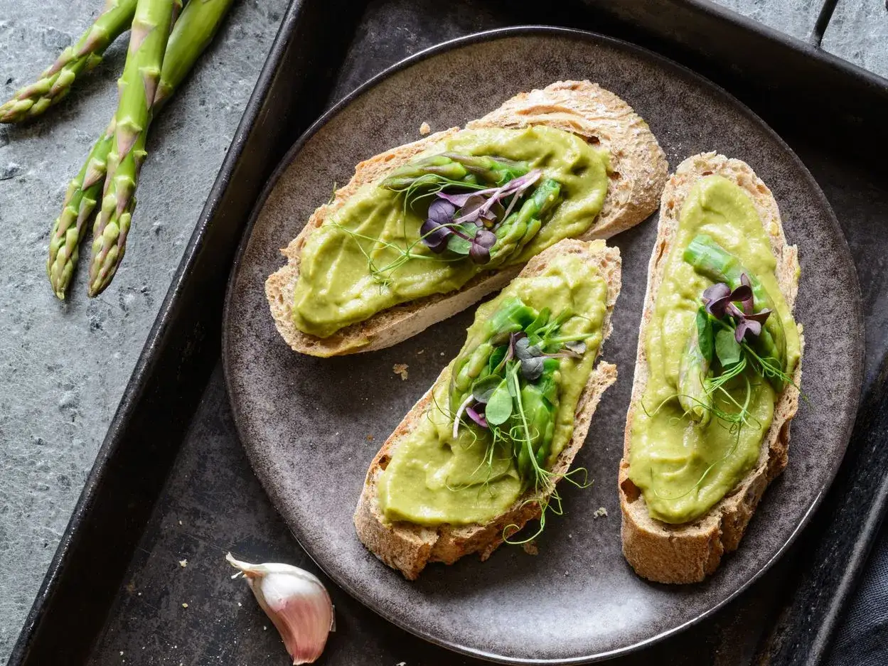 Bruschette con crema di asparagi, germogli freschi e un tocco di aglio. Un antipasto leggero e gustoso.