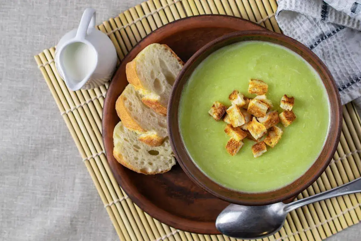 Vellutata di zucchine cremosa, guarnita con crostini dorati, servita con pane fresco e una caraffa di latte.