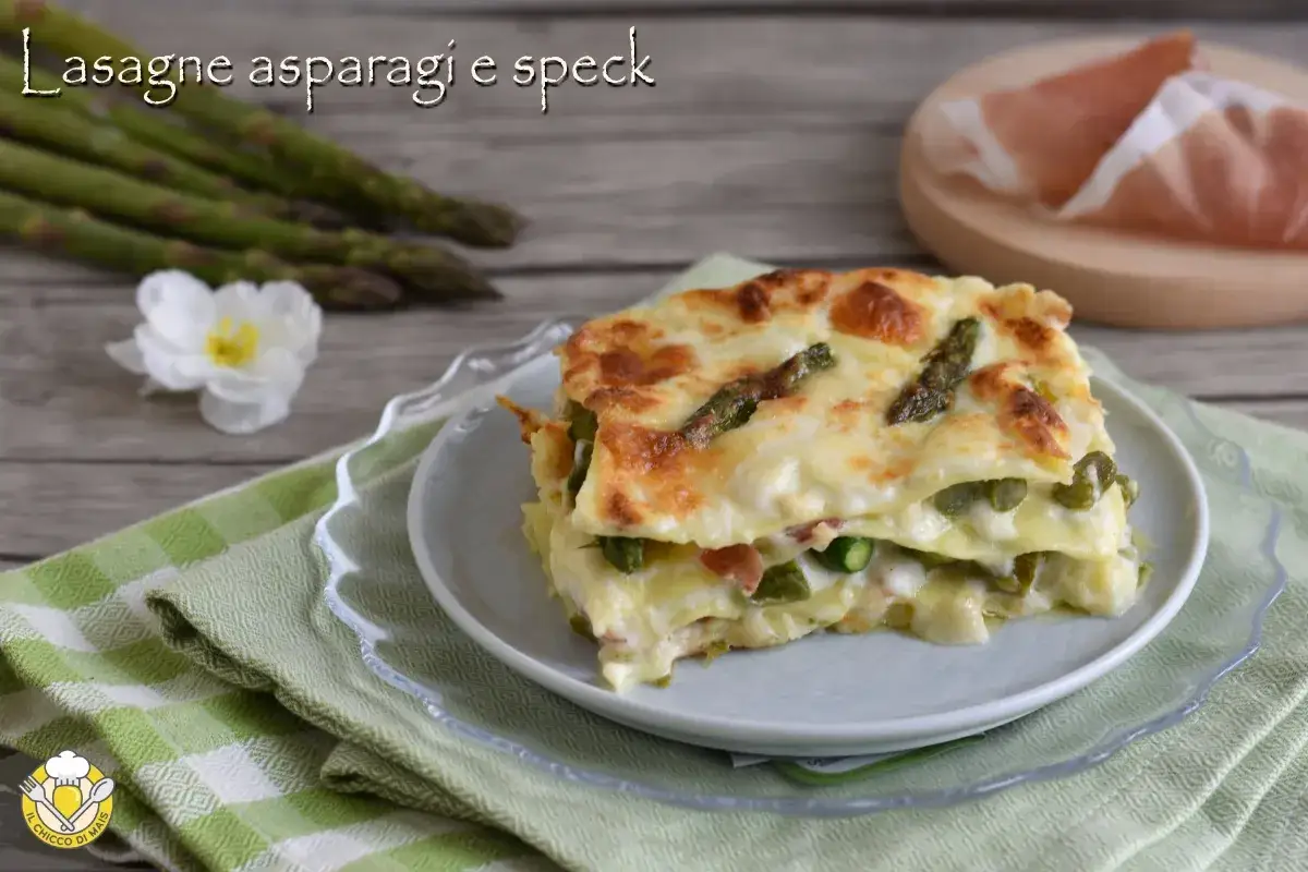 Una fetta di lasagne con asparagi e speck, dorata al forno, su un piatto con tovagliolo verde.