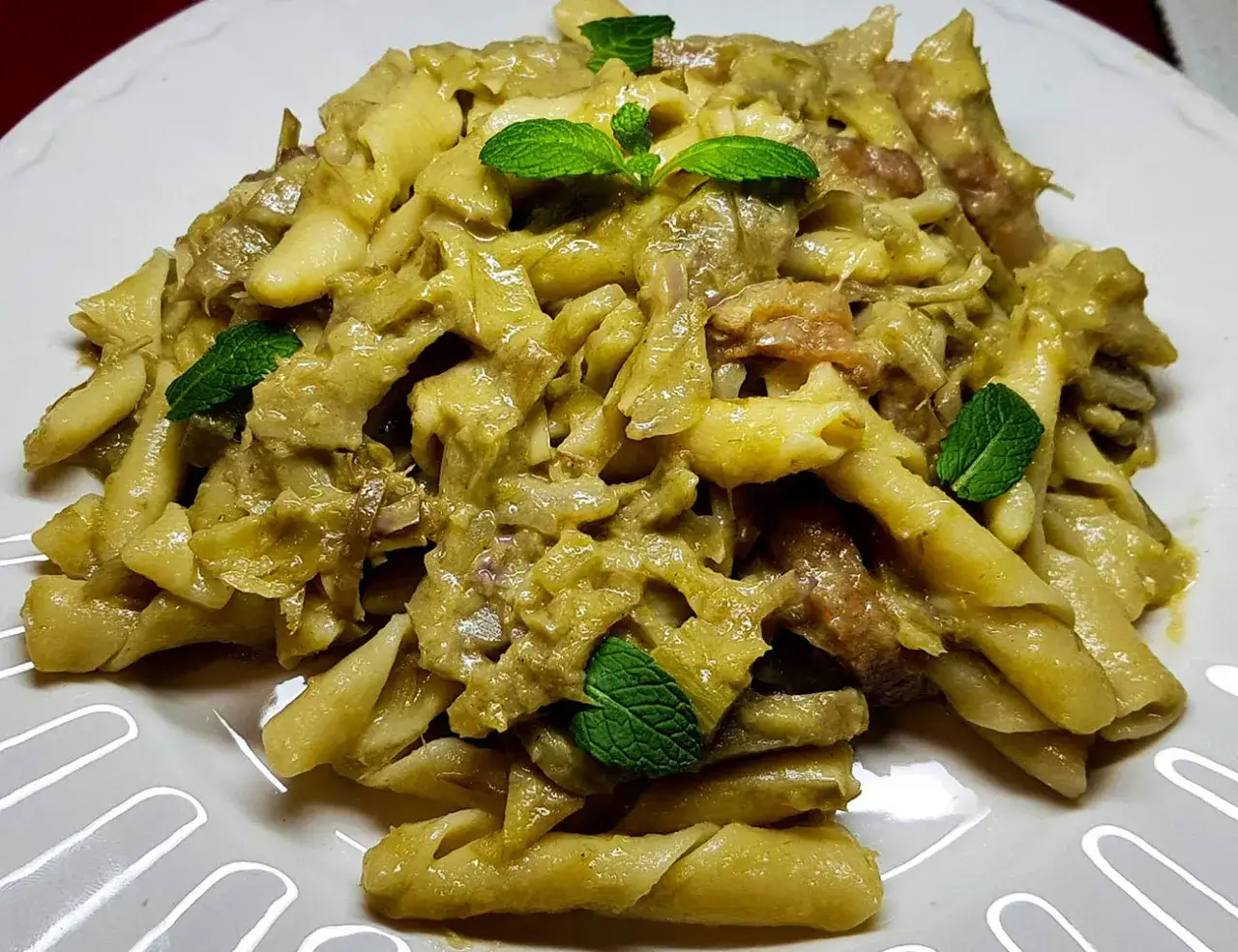 Pasta con carciofi alla siciliana, un piatto ricco e saporito, guarnito con foglie di menta fresca.