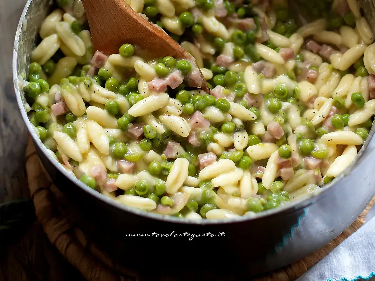 Un primo piatto cremoso di pasta e piselli con cubetti di prosciutto cotto, pronto per essere gustato.