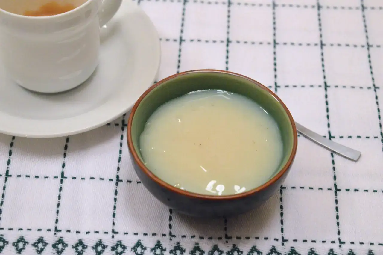 Latte condensato fatto in casa con il Bimby, servito in una ciotolina, accanto a una tazza di caffè.