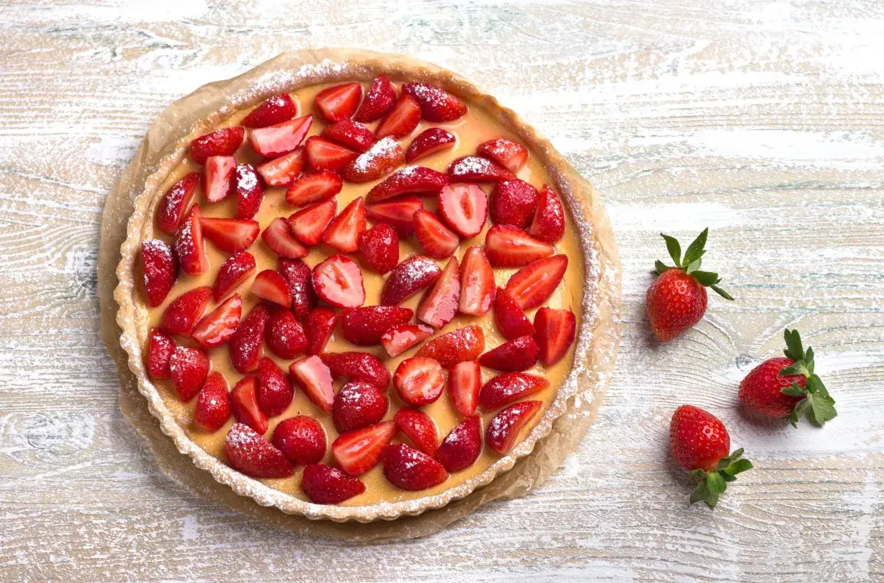 Sbriciolata alle fragole, una delizia con fragole fresche e crema, cosparsa di zucchero a velo su un tavolo di legno.