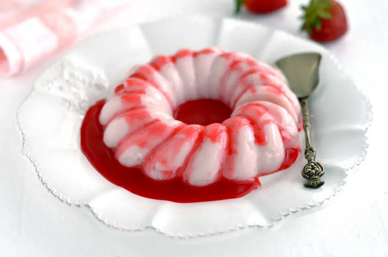 Dolce bianco a forma di ciambella, decorato con striature rosse e immerso in un delizioso coulis di fragole.
