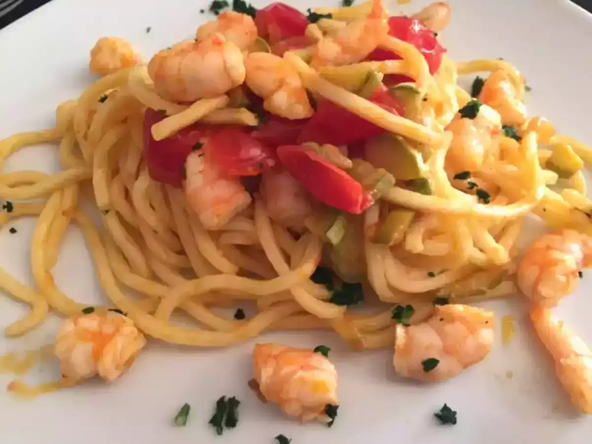 Un piatto invitante di pasta con gamberetti, pomodorini e zucchine, guarnito con prezzemolo fresco.